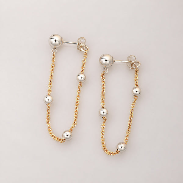 A pair of gold and silver drop earrings with small spherical beads on a light gray background.
