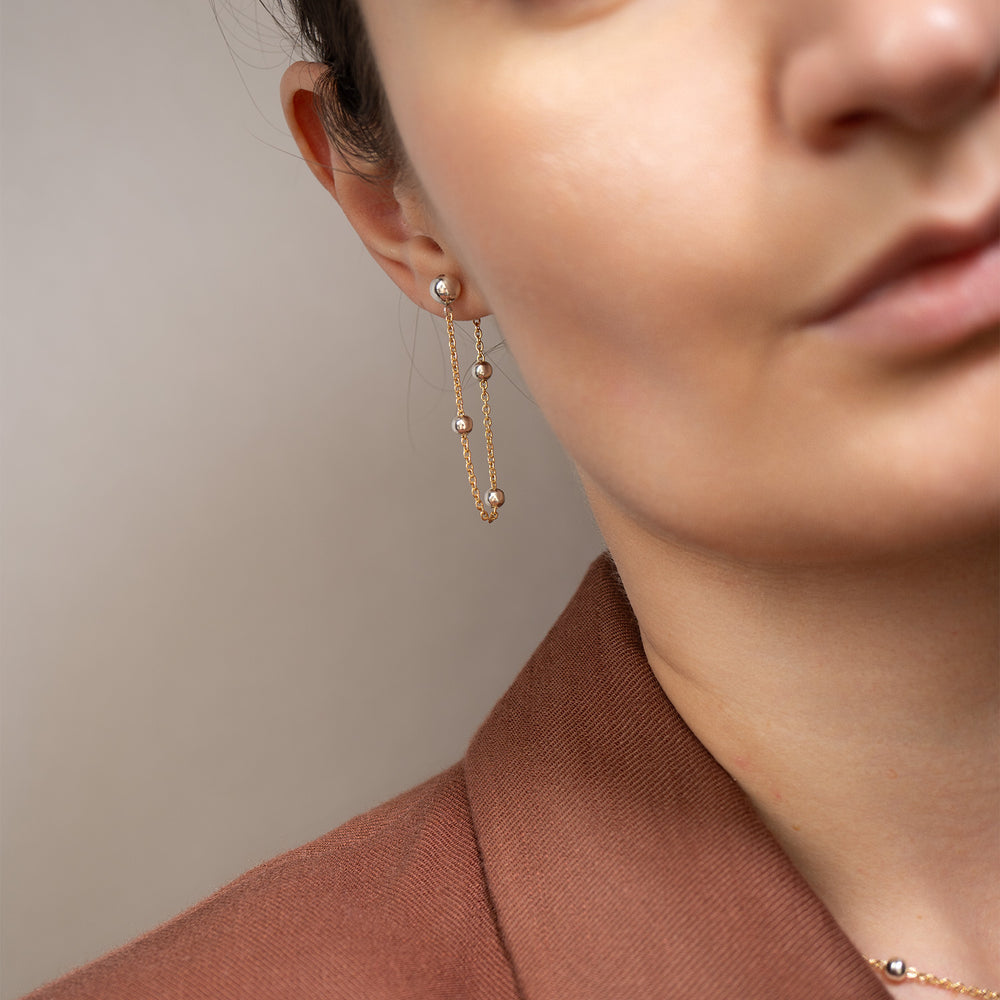 A pair of gold and silver drop earrings with spherical beads and delicate chains, displayed on a clean off-white background.