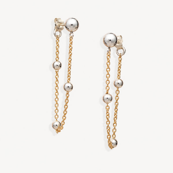 A pair of gold and silver drop earrings with spherical beads and delicate chains, displayed on a clean off-white background.