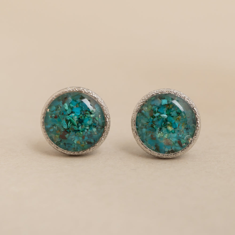 
                      
                        Pair of round earrings with turquoise stone centers on a beige background
                      
                    
