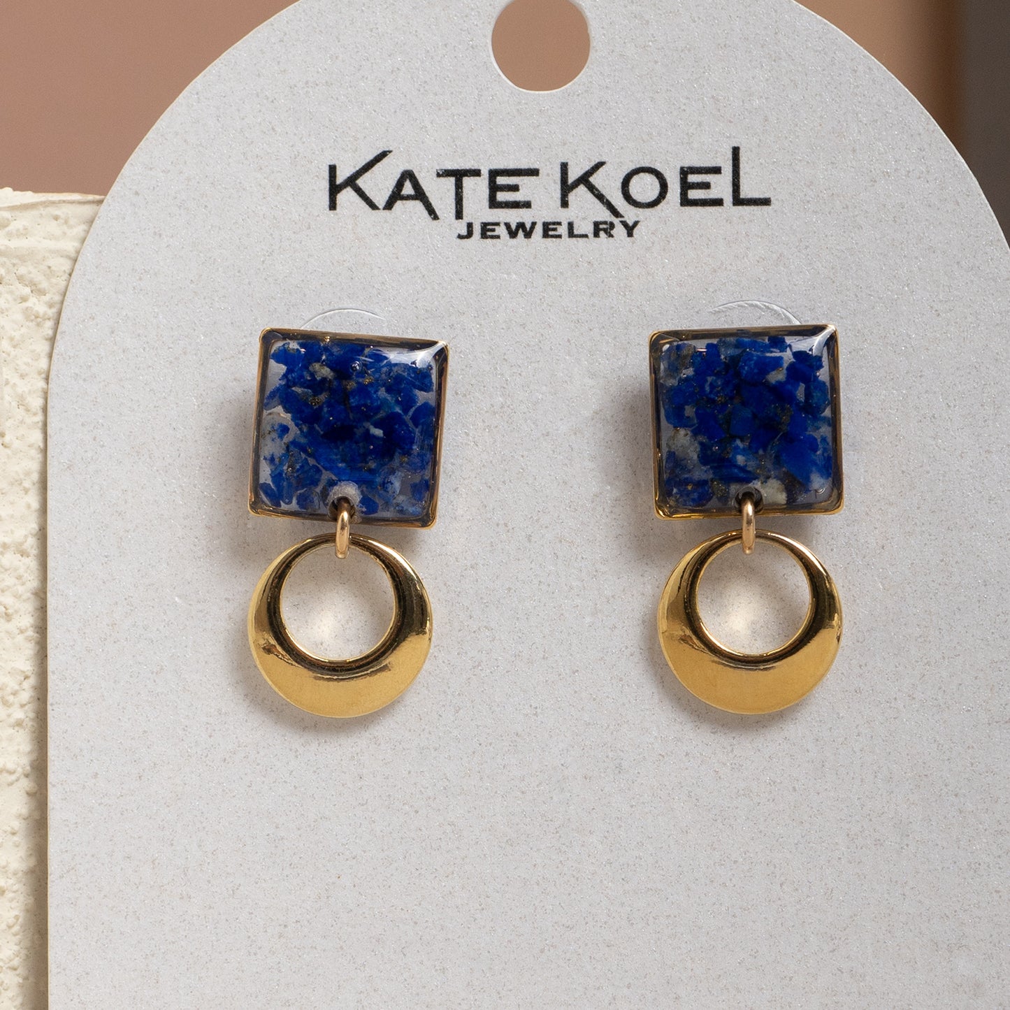Pair of earrings with blue and gold design on a Kate Koel Jewelry card.