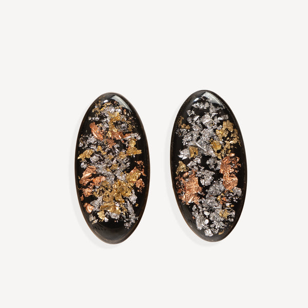 Two oval black cabochon gemstones filled with metallic gold, silver, and copper flakes, displayed side-by-side on a light gray background.