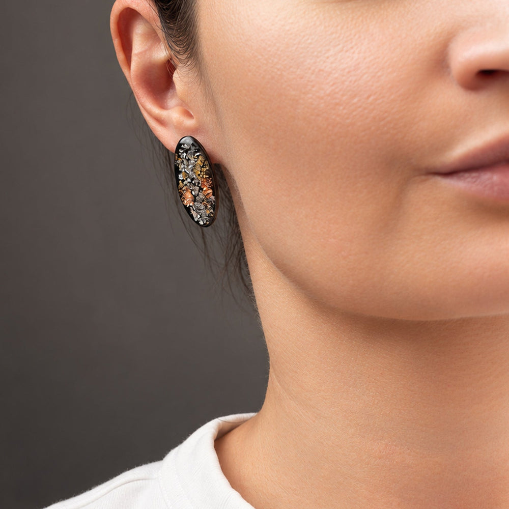 Two oval black cabochon gemstones filled with metallic gold, silver, and copper flakes, displayed side-by-side on a light gray background.