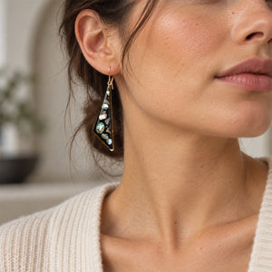 A close-up lifestyle shot of a woman wearing a gold geometric dangle earring with a black, white, and green mother-of-pearl inlay.