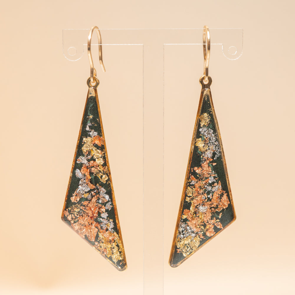 A pair of gold-tone geometric drop earrings with triangular pendants featuring a dark green background and a textured, metallic orange, gold, and silver inlay, shown against a plain off-white background.