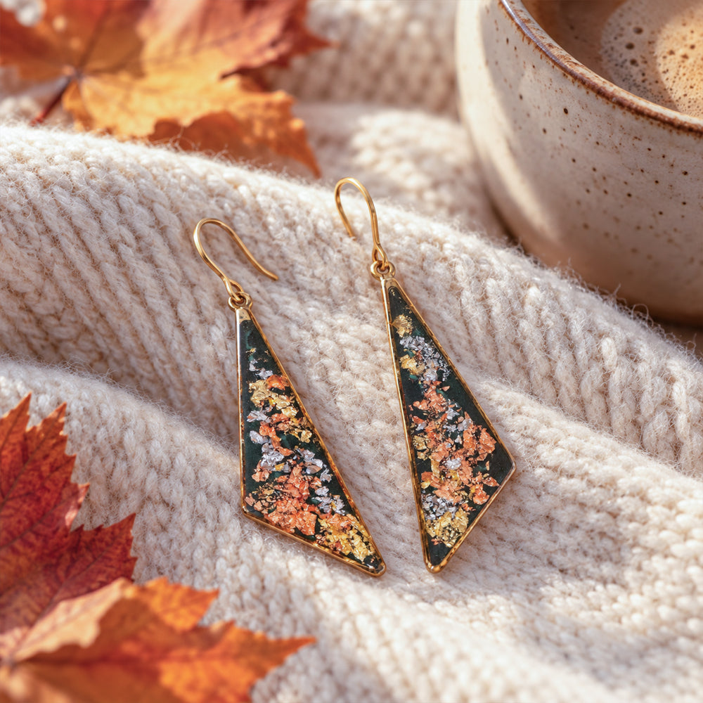 A pair of gold-tone geometric drop earrings with triangular pendants featuring a dark green background and a textured, metallic orange, gold, and silver inlay, shown against a plain off-white background.