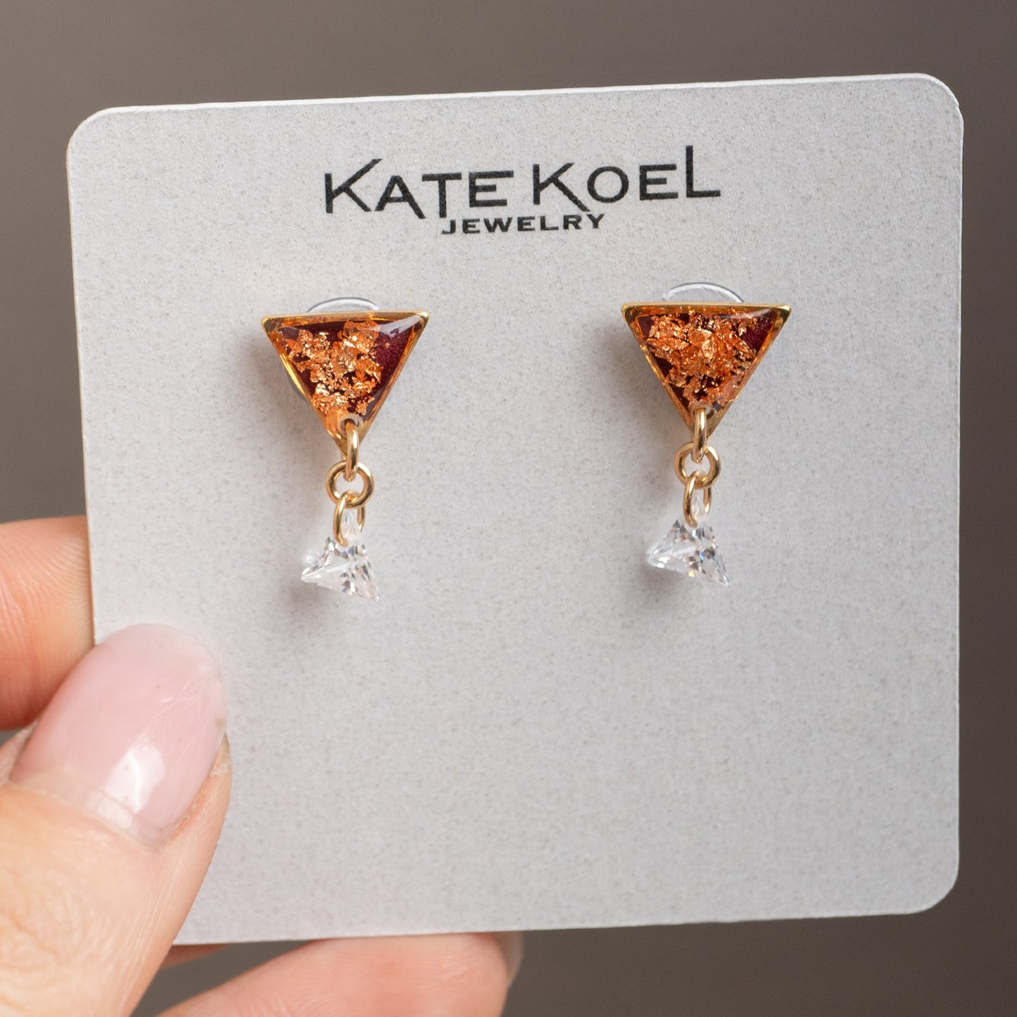 Triangle-shaped earrings on a Kate Koel Jewelry card held by a hand.