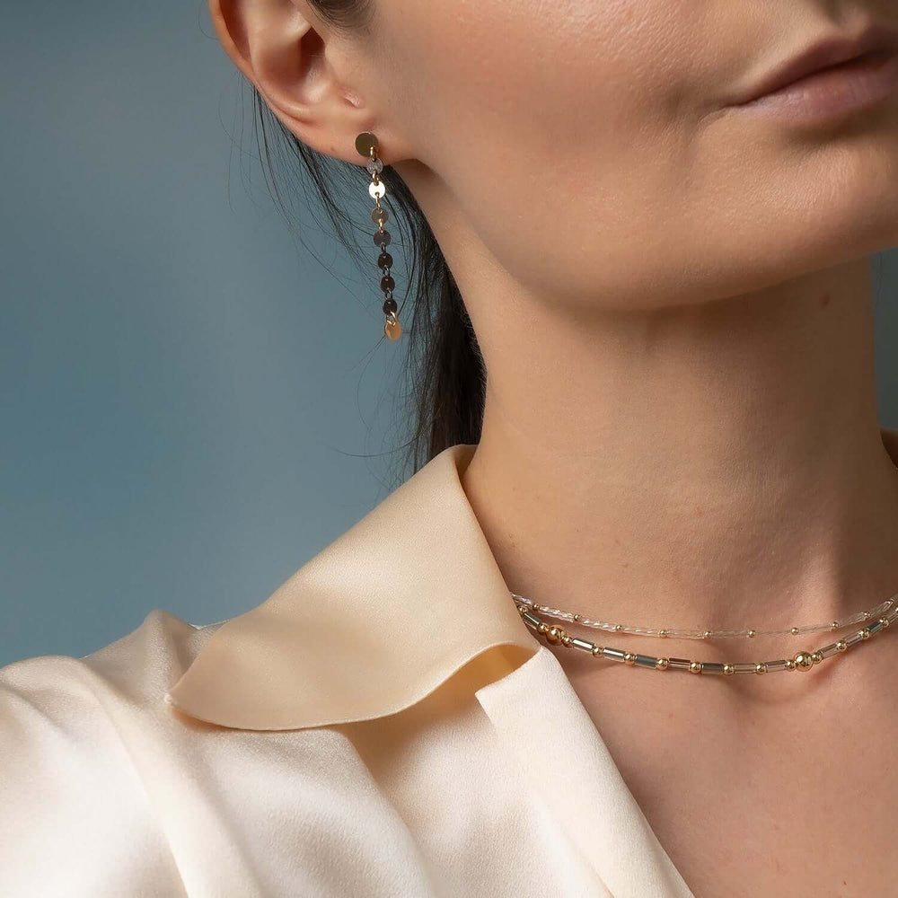 Close-up of a person wearing gold earrings and a necklace against a blue background