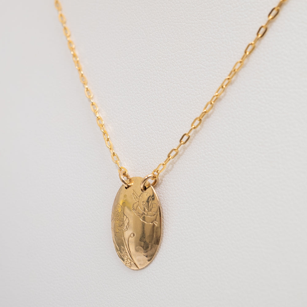 A gold oval pendant necklace with engraved floral details, suspended from a delicate gold chain against a light gray background.