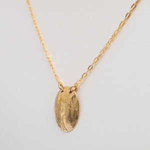 A gold oval pendant necklace with a delicate chain, displayed on a textured white background.