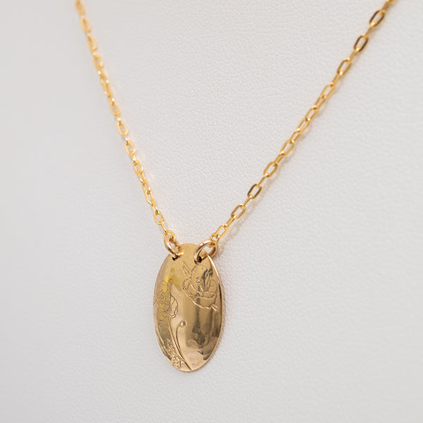 A gold oval pendant necklace with a delicate chain, displayed on a textured white background.