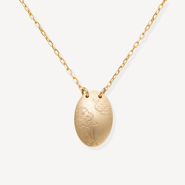 A gold oval pendant necklace with engraved floral details, suspended from a delicate gold chain against a light gray background.