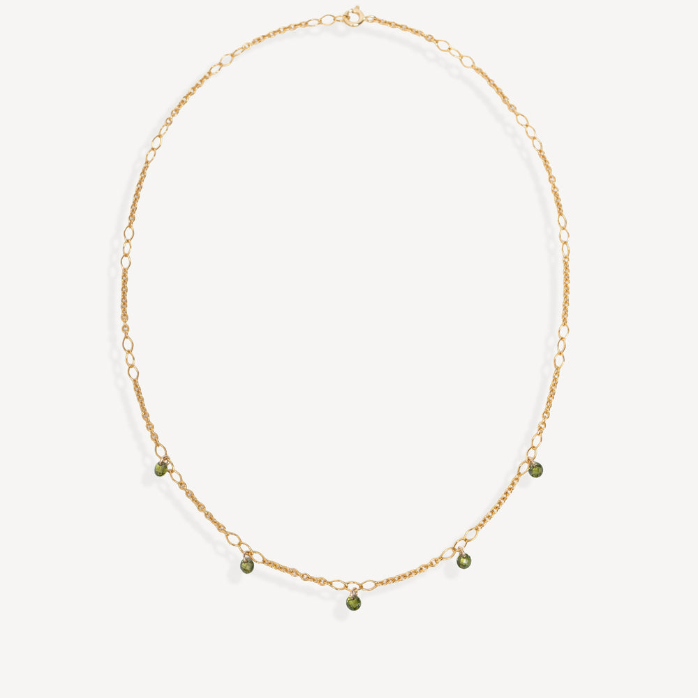 A delicate gold chain necklace with small green bead accents, displayed on a clean off-white background.