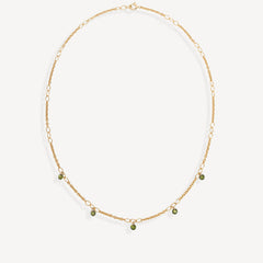 A delicate gold chain necklace with small green bead accents, displayed on a clean off-white background.