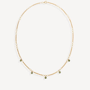 A delicate gold chain necklace with small green bead accents, displayed on a clean off-white background.