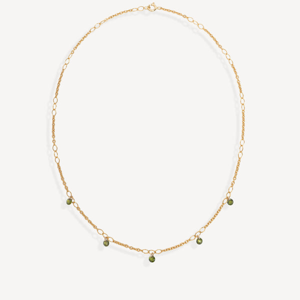 A delicate gold chain necklace with small green bead accents, displayed on a clean off-white background.
