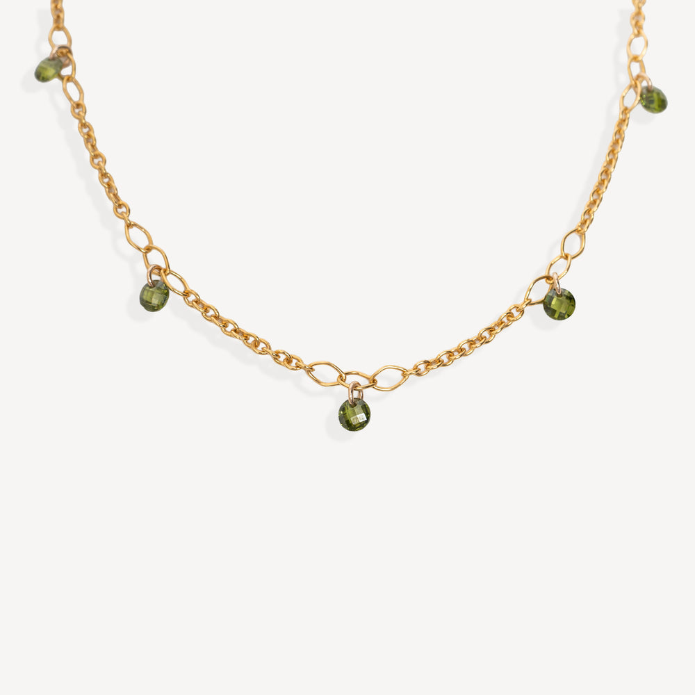 A delicate gold chain necklace with small green bead accents, displayed on a clean off-white background.