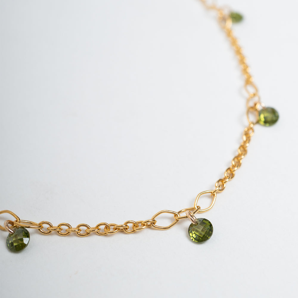 A delicate gold chain necklace with small green bead accents, displayed on a clean off-white background.