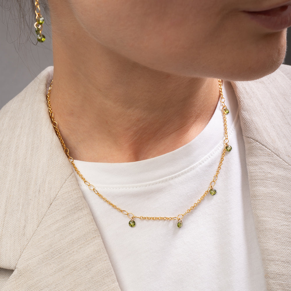 A delicate gold chain necklace with small green bead accents, displayed on a clean off-white background.