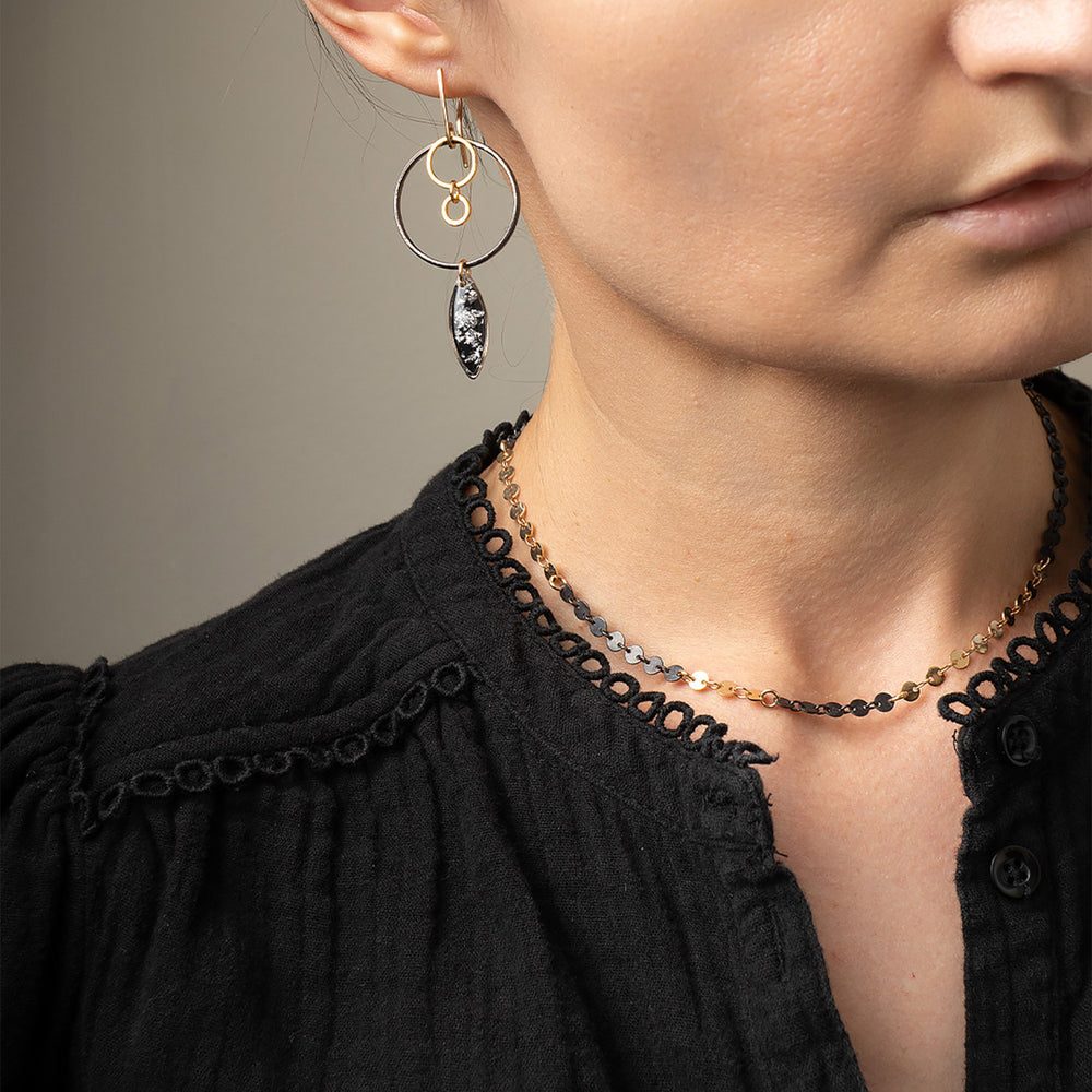
                      
                        Close-up of a person wearing gold hoop earrings and a necklace with a neutral background
                      
                    