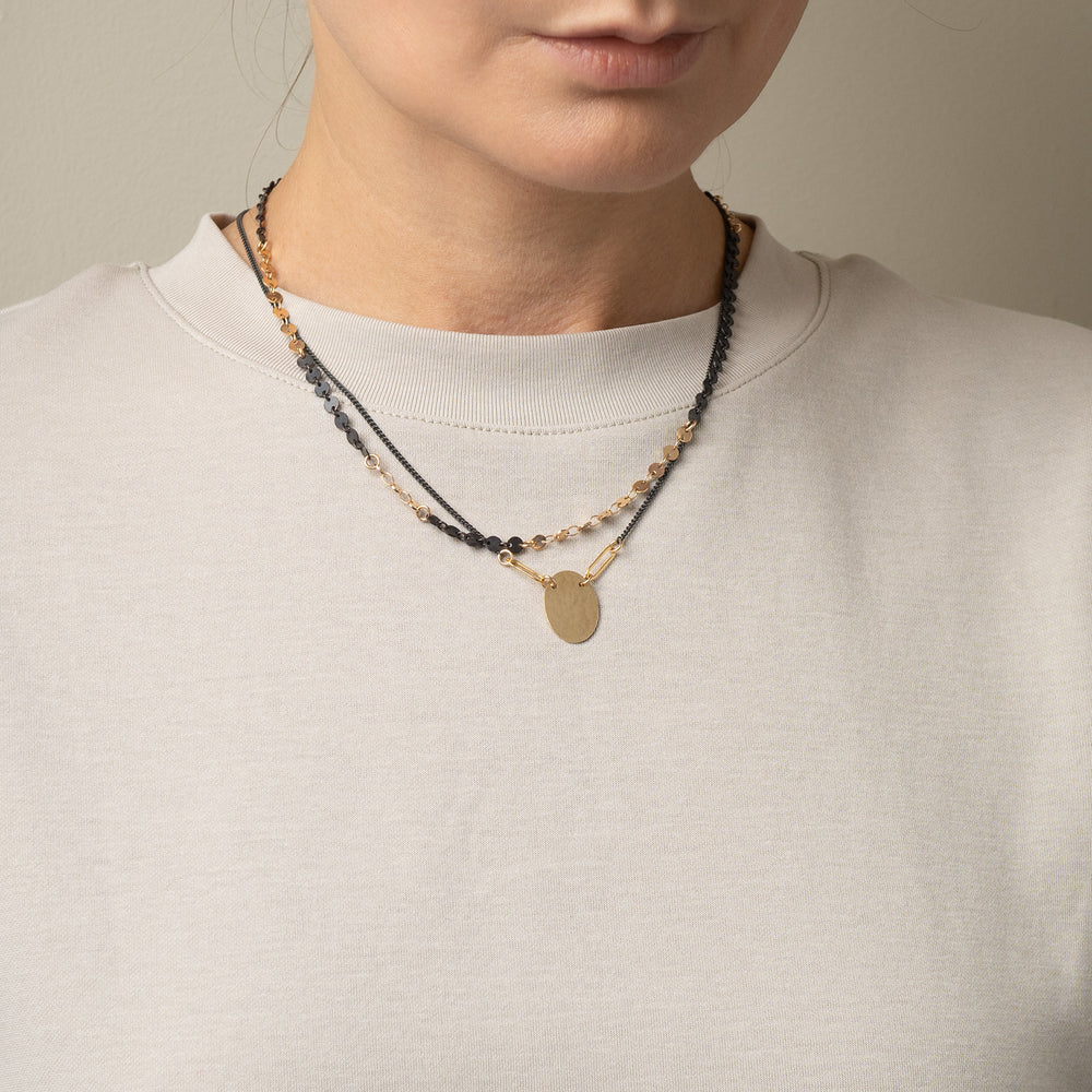 
                      
                        Necklace with gold and black beads worn by a person in a light gray sweater.
                      
                    