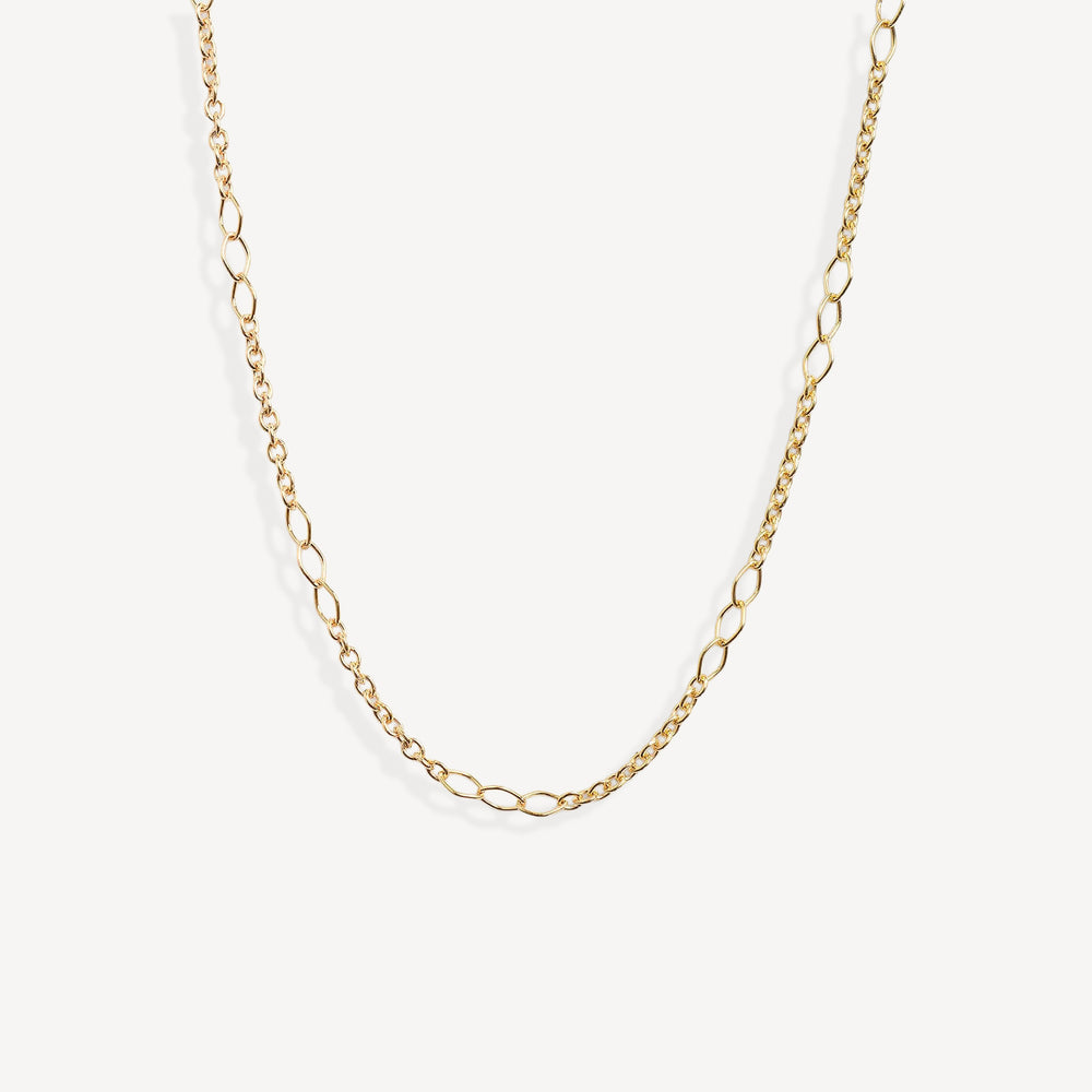 A delicate gold chain necklace with elongated oval links, displayed in a curved shape against a clean, off-white background.