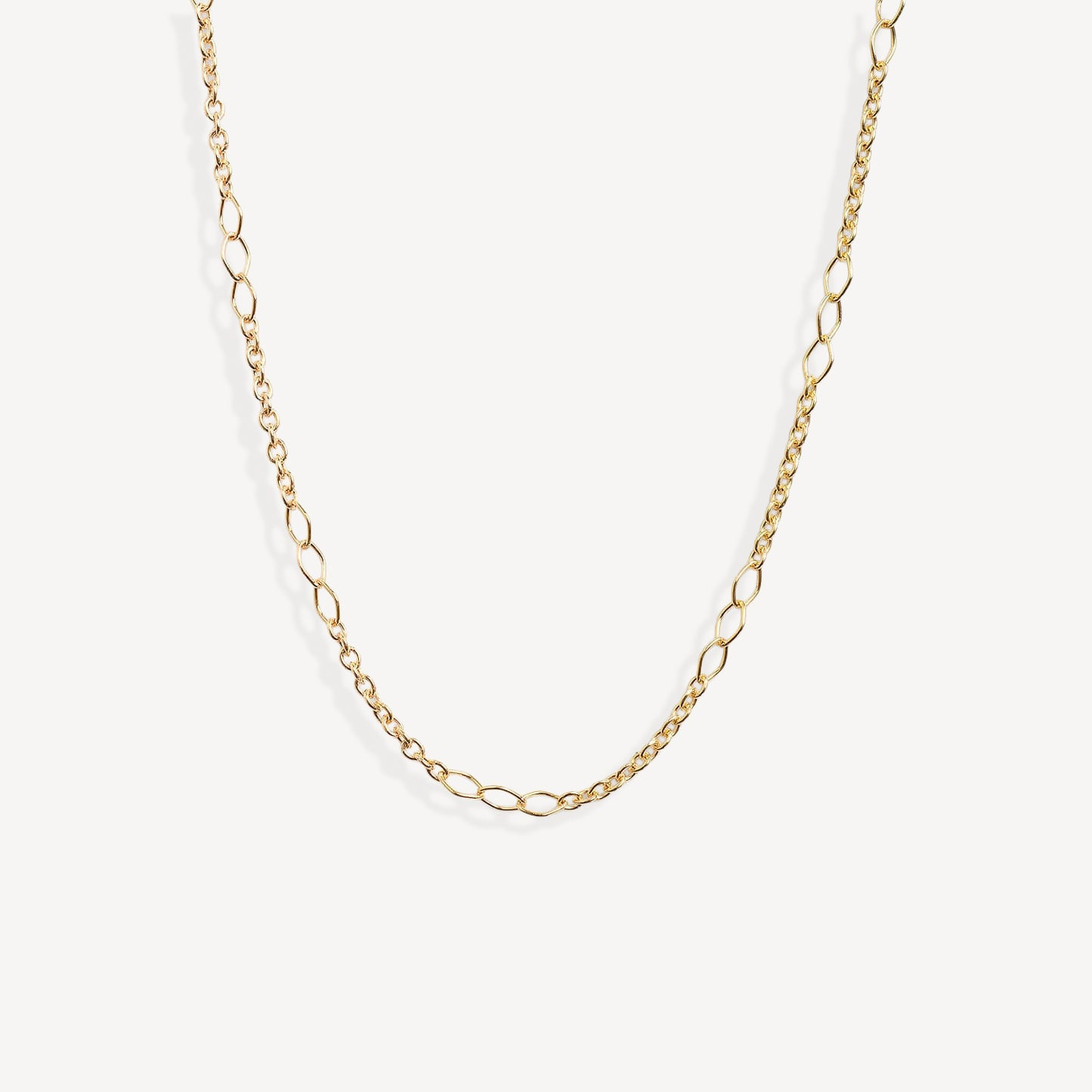 A delicate gold chain necklace with elongated oval links, displayed in a curved shape against a clean, off-white background.