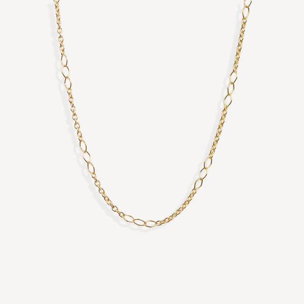 A delicate gold chain necklace with elongated oval links, displayed in a curved shape against a clean, off-white background.