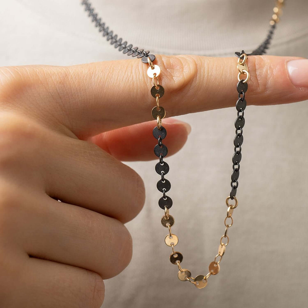 
                      
                        Two gold and black chain necklaces held between fingers against a neutral background
                      
                    