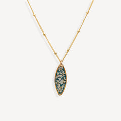 A gold chain necklace with a marquise-shaped pendant featuring a teal blue background and white floral details, shown against a light gray background.