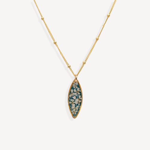 A gold chain necklace with a marquise-shaped pendant featuring a teal blue background and white floral details, shown against a light gray background.