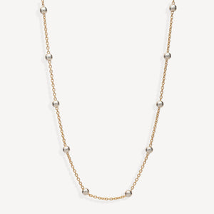 A delicate gold chain necklace featuring evenly spaced, polished silver-toned round beads, displayed against a clean off-white background.