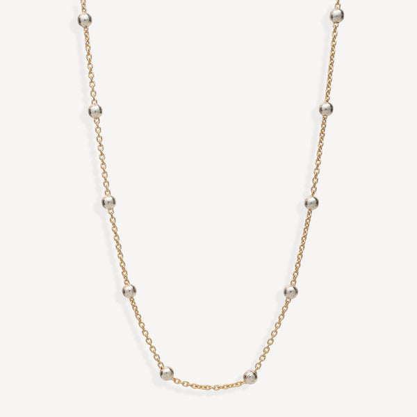 A delicate gold chain necklace featuring evenly spaced, polished silver-toned round beads, displayed against a clean off-white background.