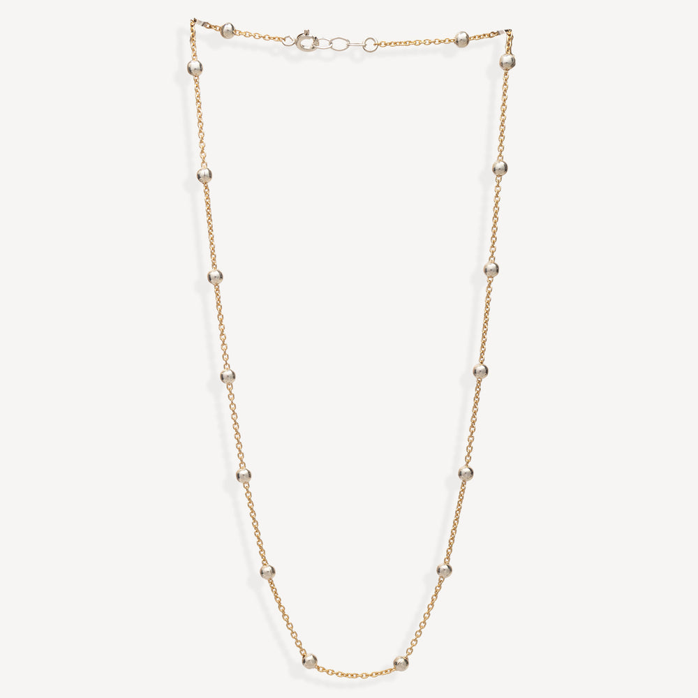 A delicate gold chain necklace featuring evenly spaced, polished silver-toned round beads, displayed against a clean off-white background.