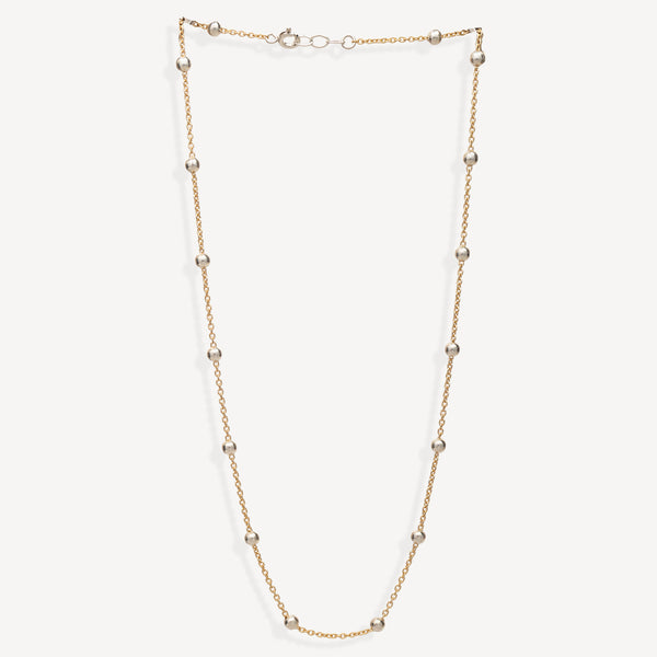 A delicate gold chain necklace featuring evenly spaced, polished metallic beads, displayed against a clean, off-white background.