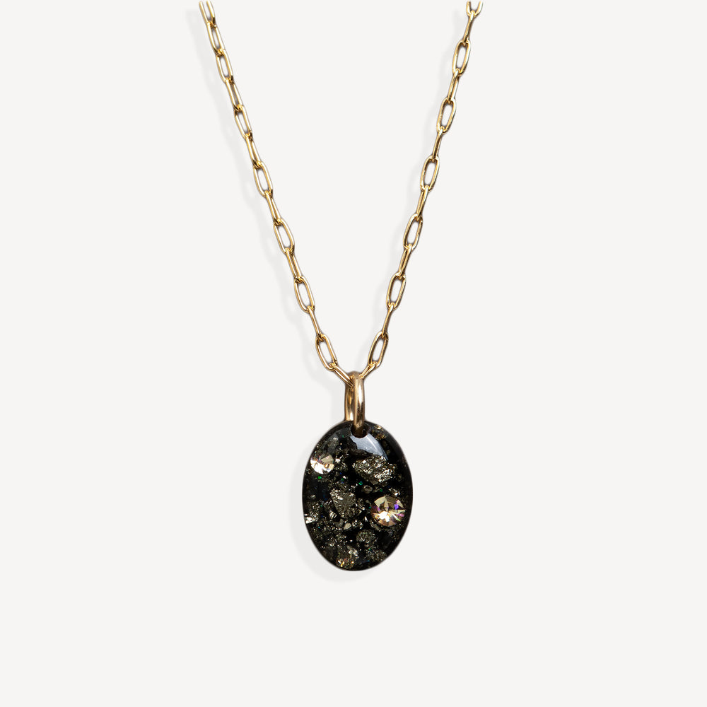 Gold chain necklace with an oval pendant containing black mineral inclusions and a small iridescent stone, shown on a light gray background.