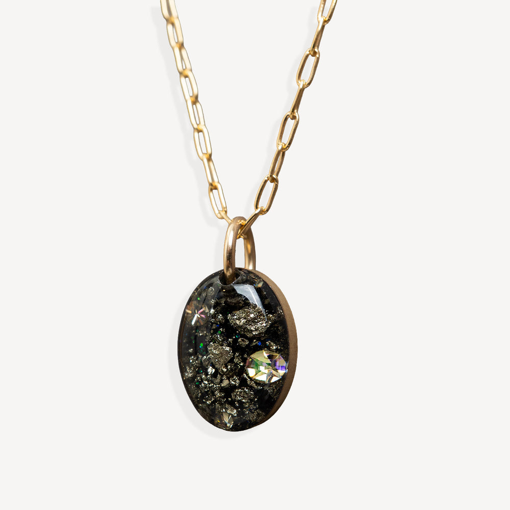 Gold chain necklace with an oval pendant containing black mineral inclusions and a small iridescent stone, shown on a light gray background.