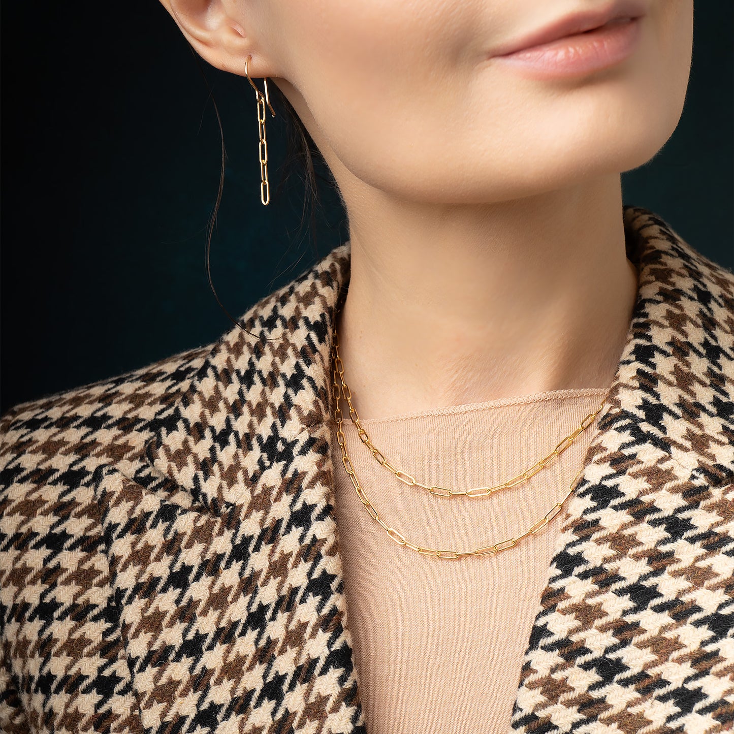 Close-up of a person wearing gold chain necklaces and earrings against a dark background