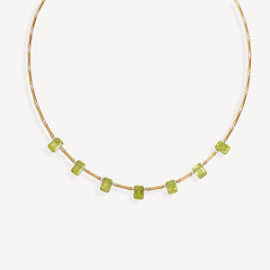 A delicate gold chain necklace featuring a row of small, faceted green gemstones spaced along the front, displayed against a clean, light off-white background.
