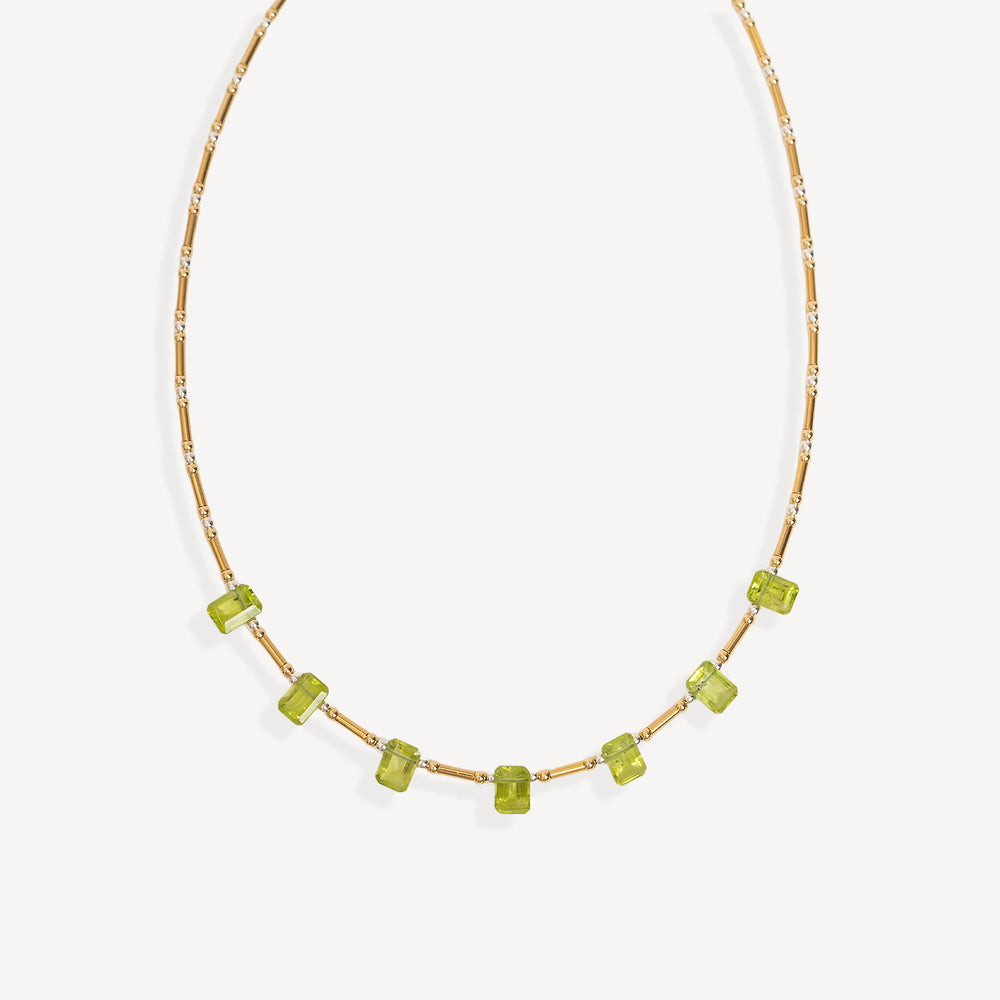 A delicate gold chain necklace featuring a row of small, faceted lime green gemstone beads, displayed against a clean off-white background.