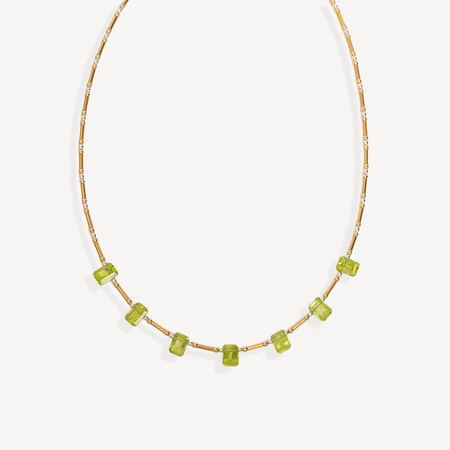 A delicate gold chain necklace featuring a row of small, faceted lime green gemstone beads, displayed against a clean off-white background.