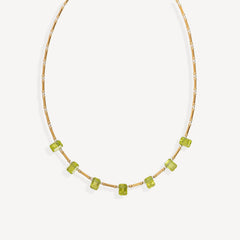 A delicate gold chain necklace featuring a row of small, faceted lime green gemstone beads, displayed against a clean off-white background.