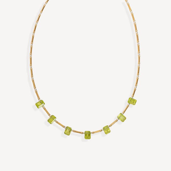 A delicate gold chain necklace featuring a row of small, faceted lime green gemstone beads, displayed against a clean off-white background.