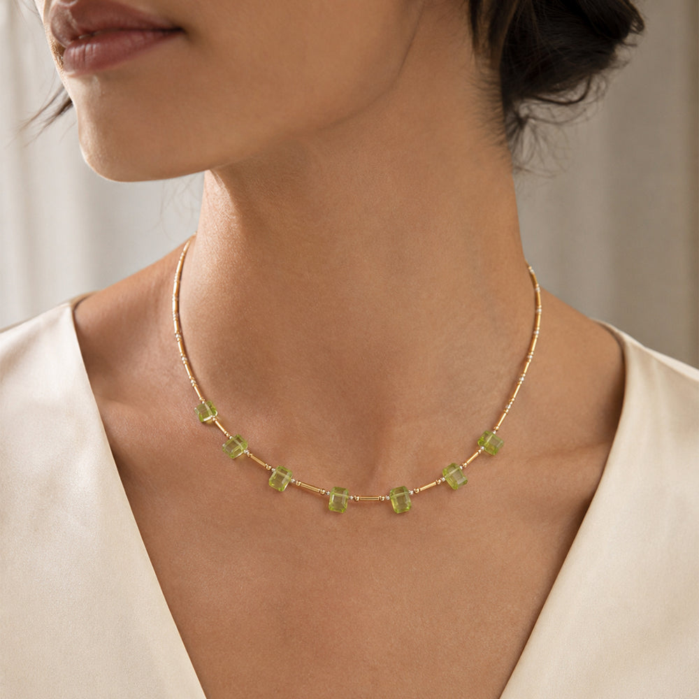 A delicate gold chain necklace featuring a row of small, faceted lime green gemstone beads, displayed against a clean off-white background.