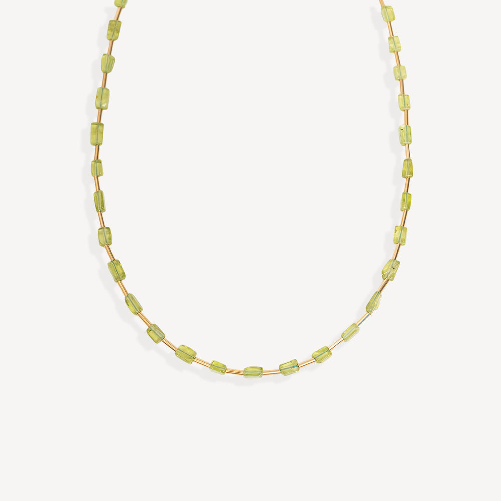 A delicate gold chain necklace featuring small, faceted light green gemstone beads, photographed against a clean off-white background.