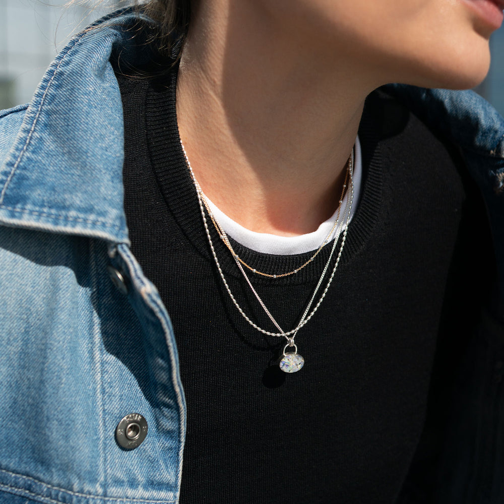 Person wearing layered necklaces with a denim jacket and black shirt