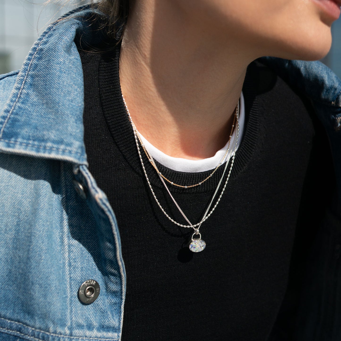 Person wearing layered necklaces with a denim jacket and black shirt
