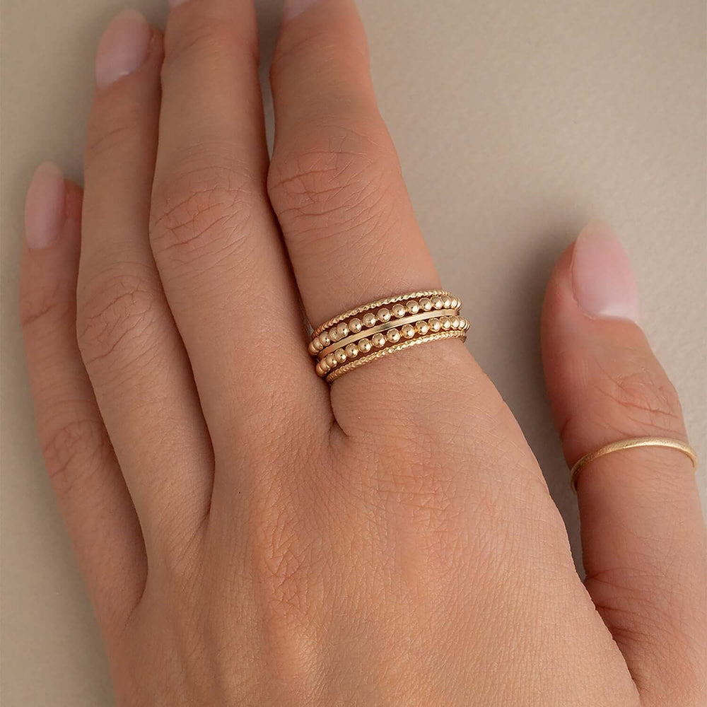 
                      
                        Hand wearing two gold rings on a neutral background
                      
                    