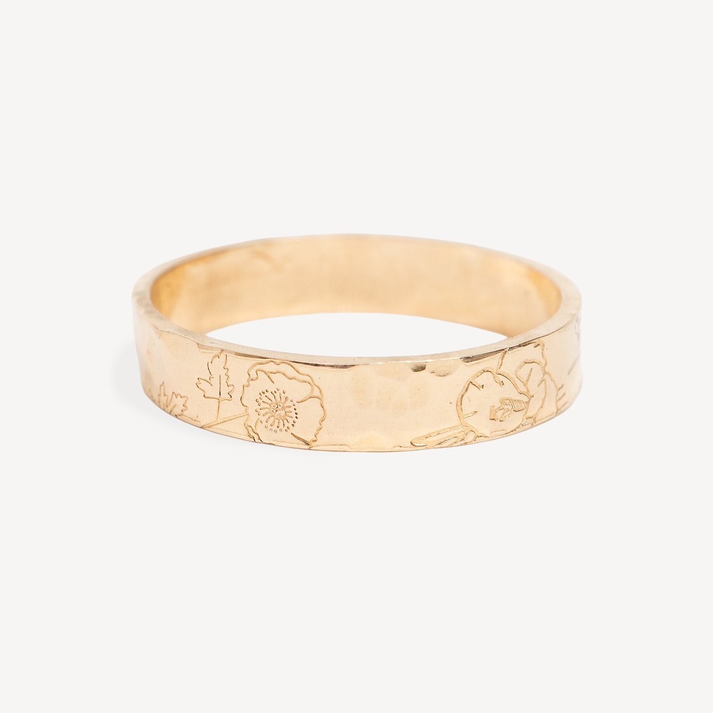 A gold band ring with a hammered texture and engraved floral patterns, shown on a light gray background.