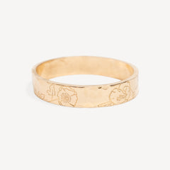A gold band ring with a hammered texture and engraved floral patterns, shown on a light gray background.